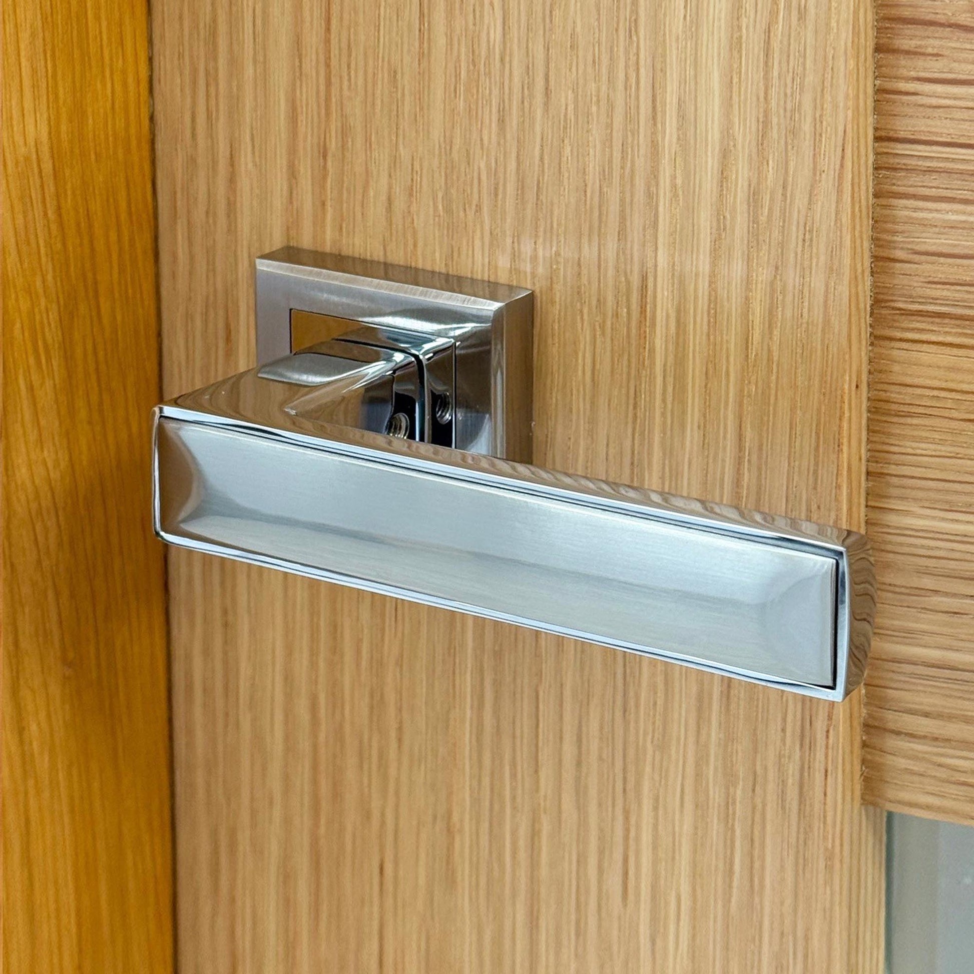 Close-up of a modern Alto Handle silver door handle on a oak wooden door