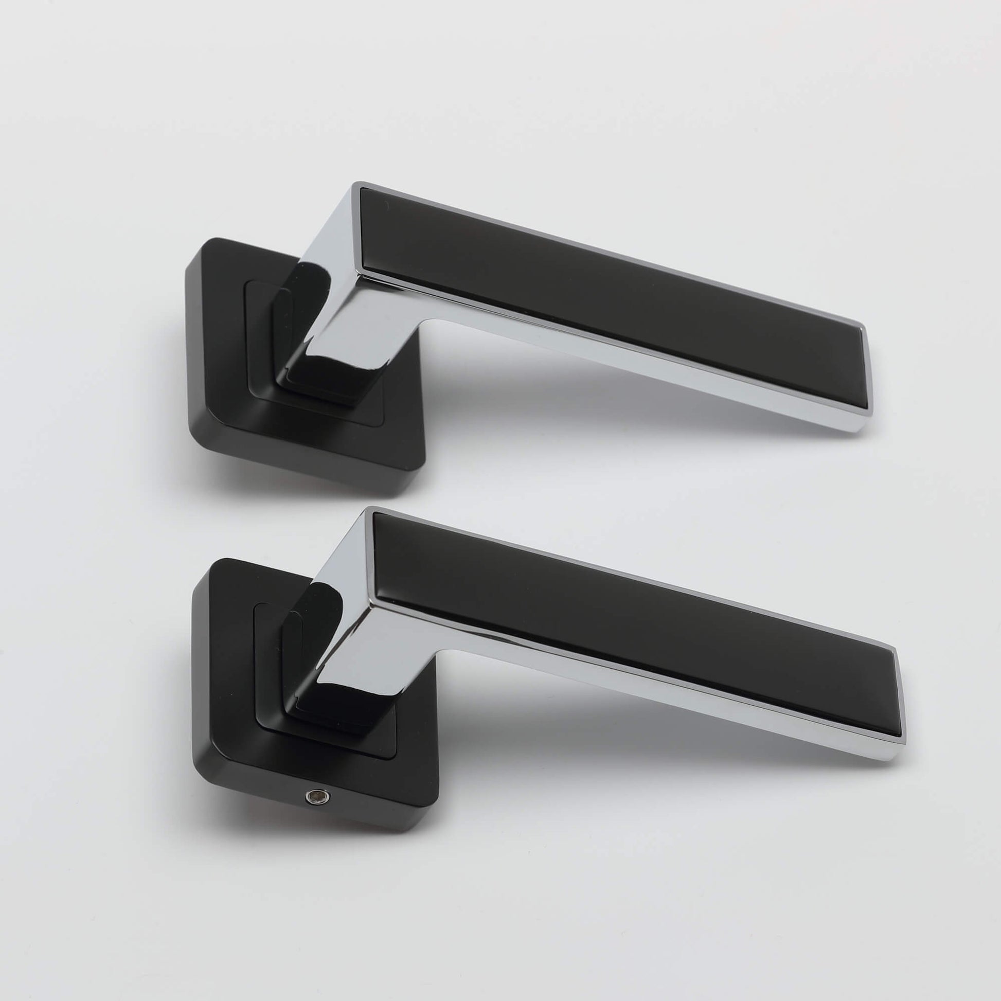 A side view of a  pair of Alto flat black & chrome plated square rose door handles on a white background.