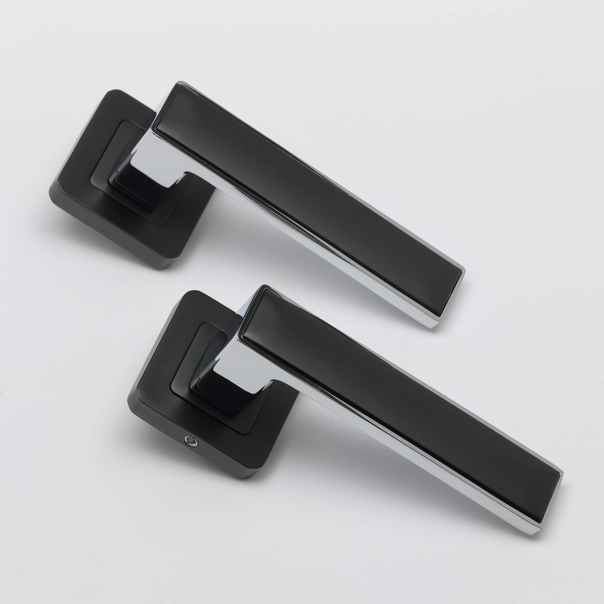 An angled view of a pair Alto flat black & chrome plated square rose door handles on a white background.