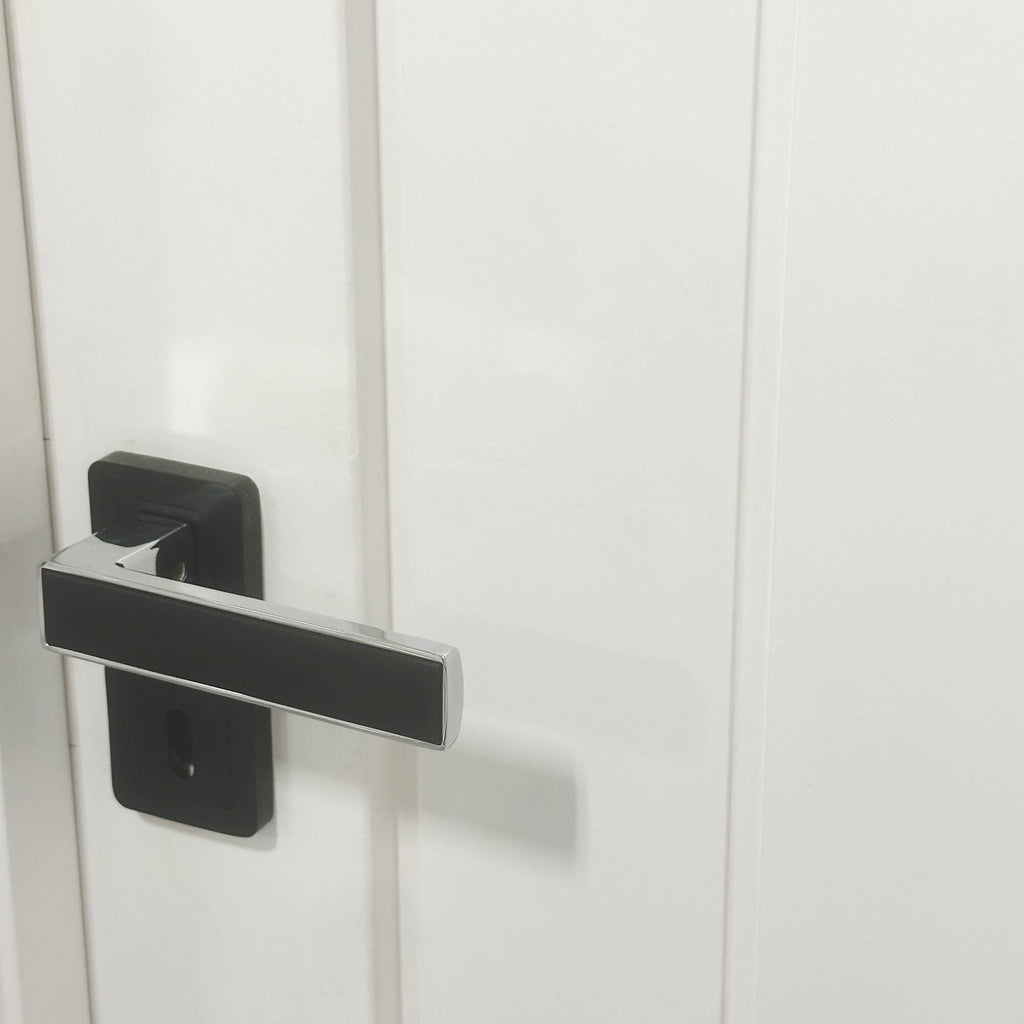 A Alto Flat Black & Chrome Plated Square Rose door handle on a white door