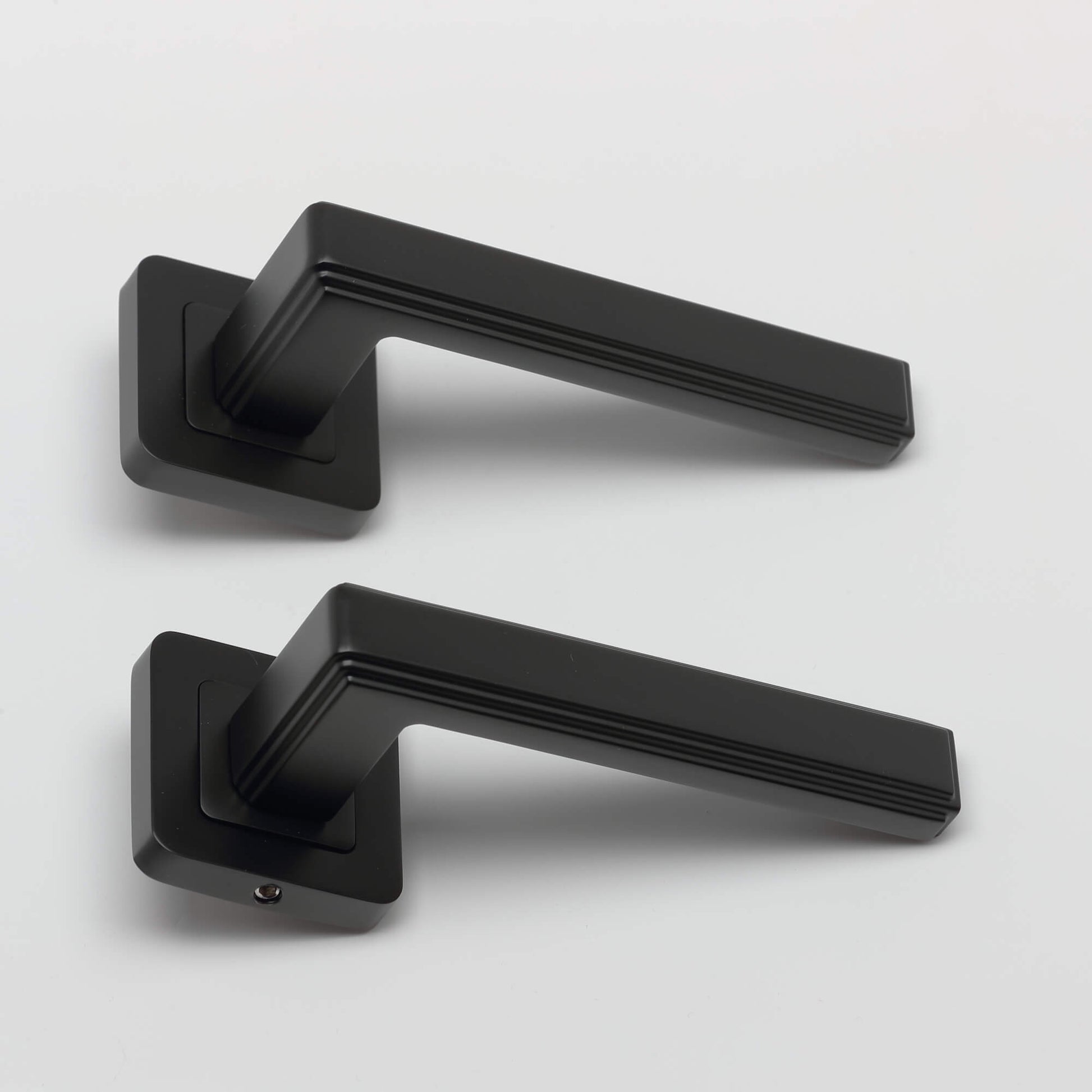 A pair of Ares Flat Black Square Rose door handles on a grey background.