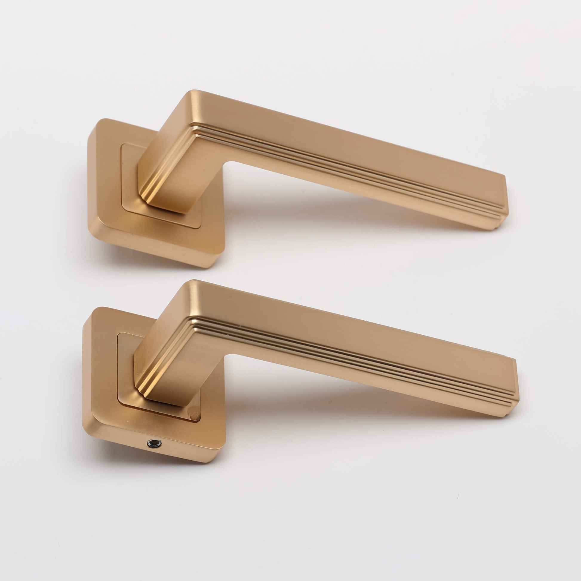 Side view of a pair of Ares Satin Brass Square Rose door handles on a grey background.