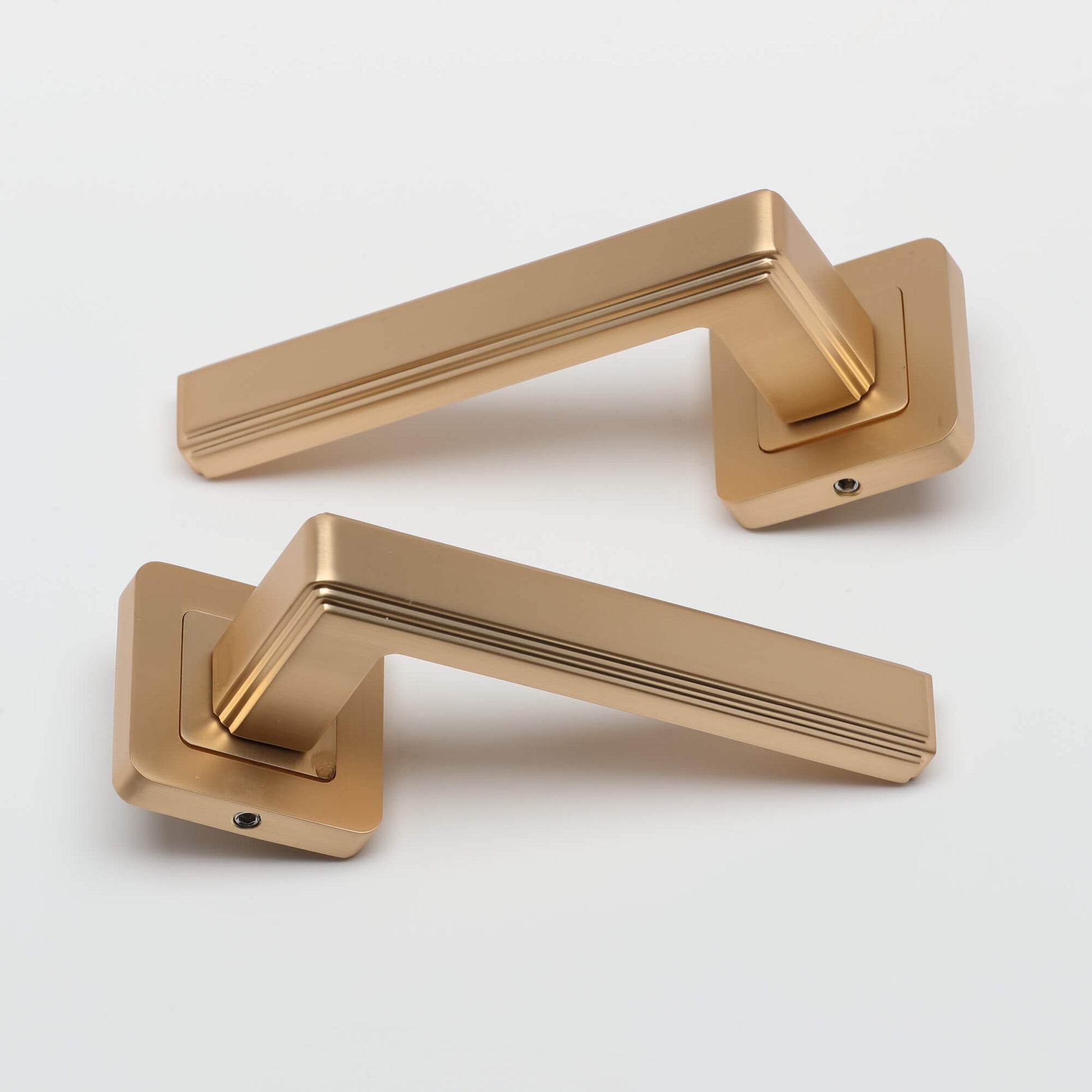 Pair of Ares Satin Brass Square Rose door handles on a grey background
