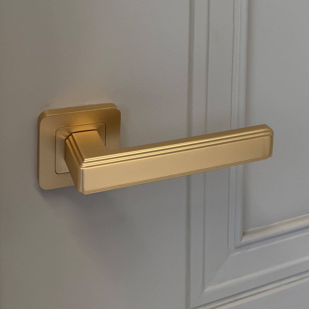 An Ares Satin Brass Square Rose door handle on a grey panelled internal door