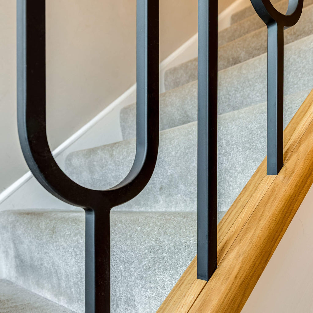 Close-up of a staircase with light grey carpeted steps, a natural wood baserail, and Black Oval Spindles.
