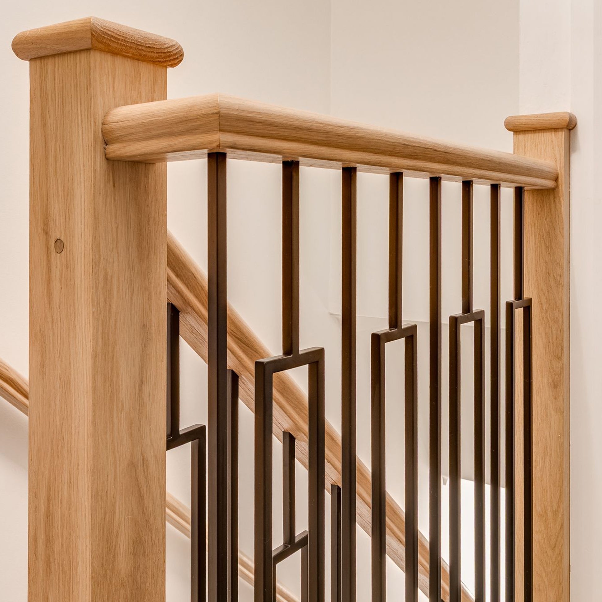 Close-up of Black Rectangle Spindles on a wooden staircase railing with a neutral background.