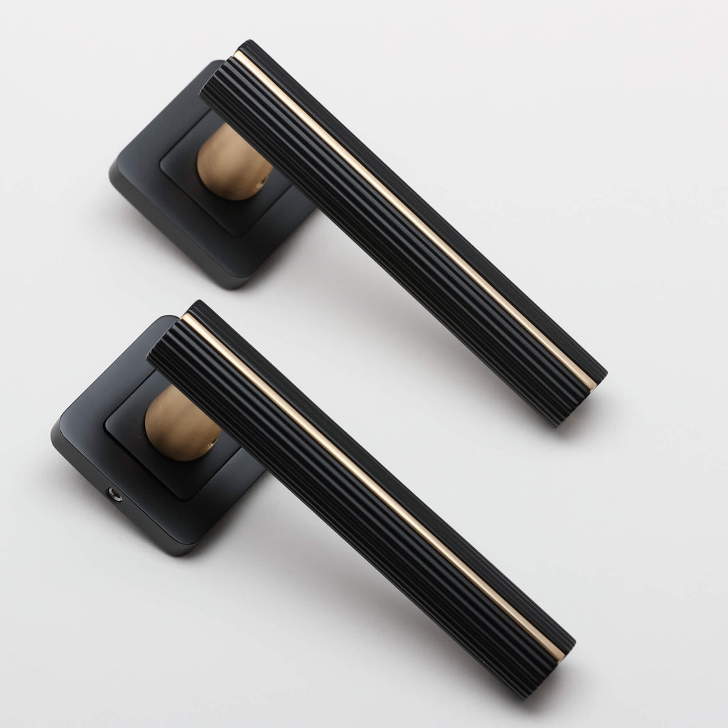 An angled view of a pair of Calvus Flat Black & Satin Brass Square Rose Handles on a light grey background.