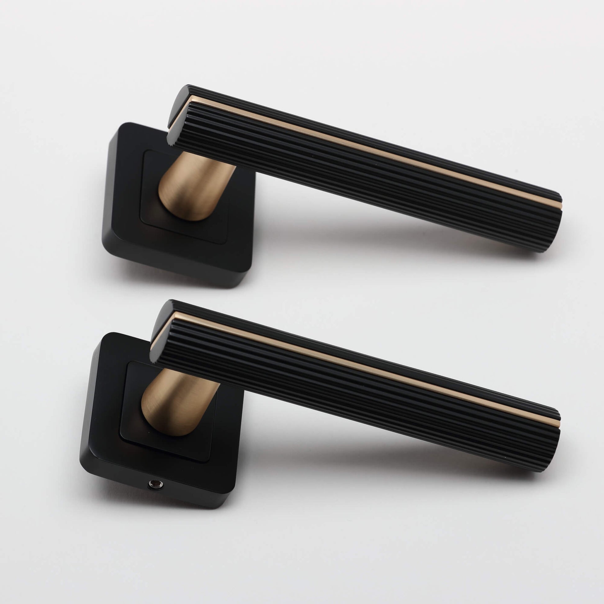 A side view of a pair of Calvus Flat Black & Satin Brass Square Rose Handles on a light grey background.