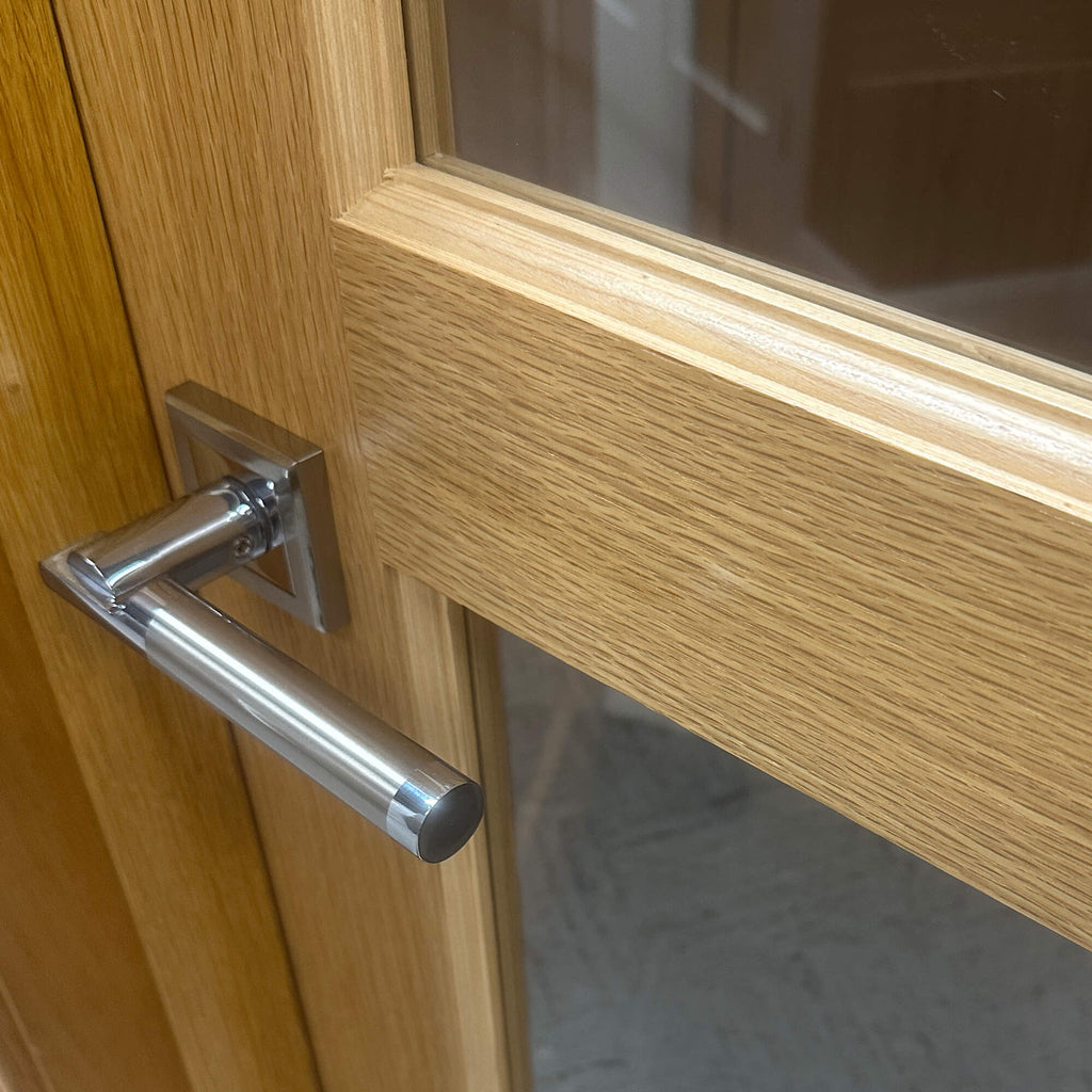 Close-up of the wood grain and a Cumulus door handle on a A Contemporary White Oak 4 Lite Unglazed Internal 40mm Door, with 4mm clear toughened glass.