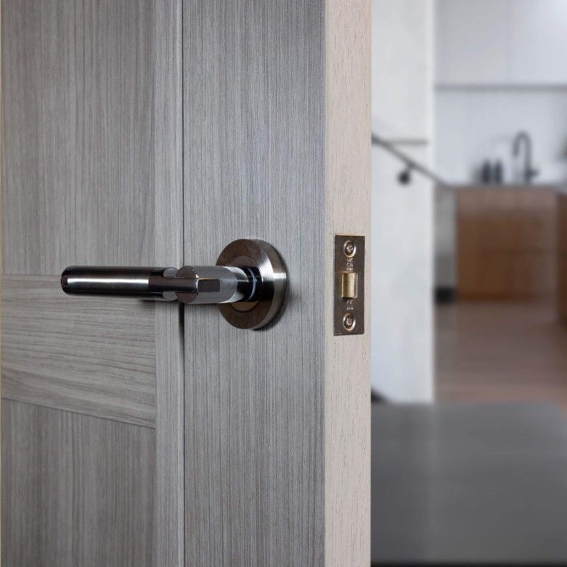 Close-up of a Cumulus Nickel Brushed & Polished Chrome Handle on a wooden door with a blurred kitchen background