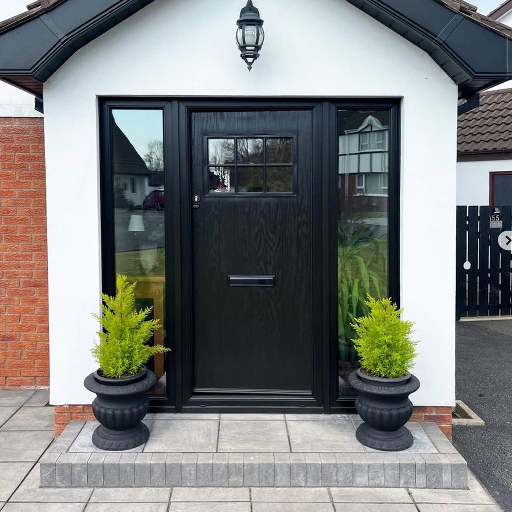A black Dublin Composite GRP External Door with clear glass panels on a white house exterior, flanked by two potted plants.