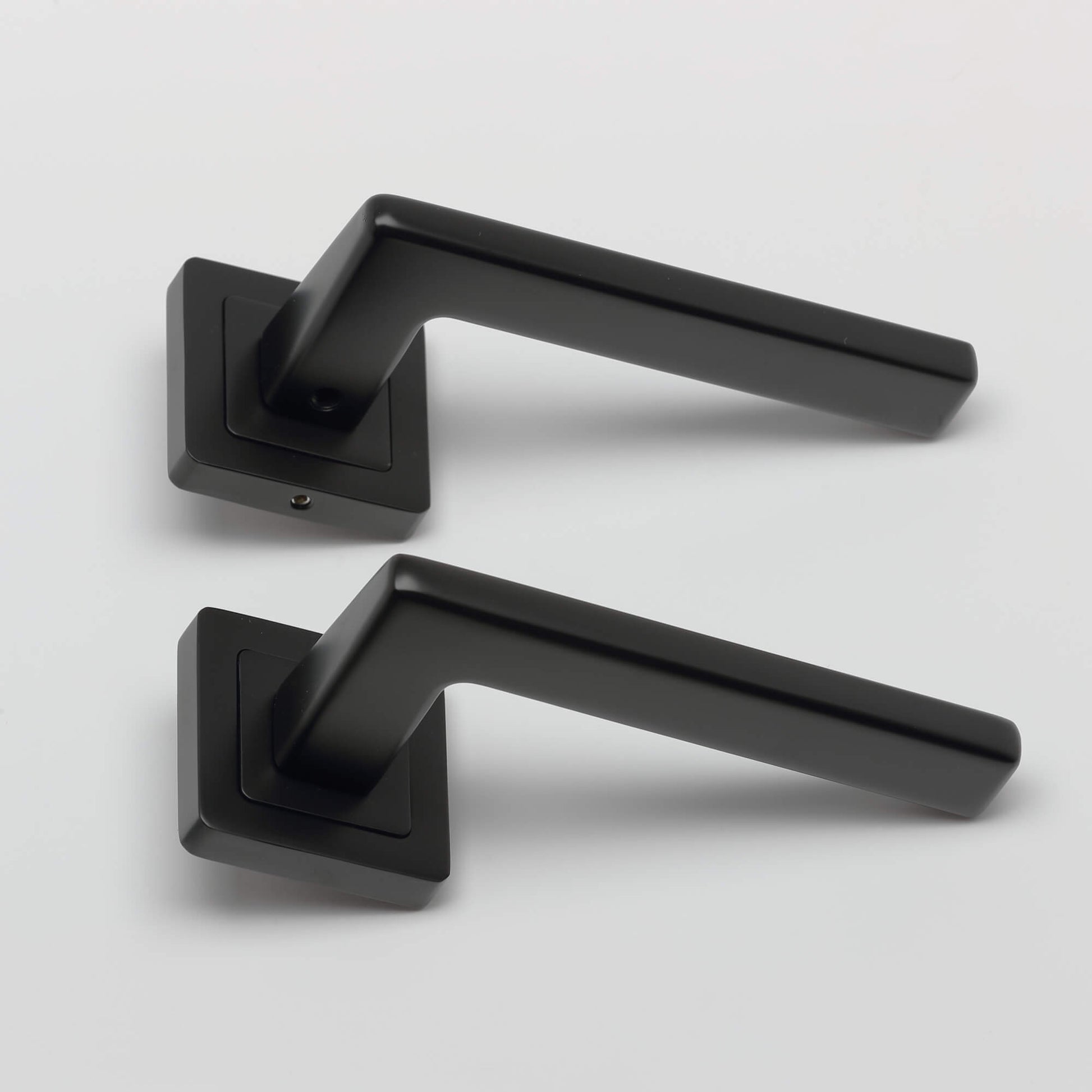 A side view of a set of Hera Flat Black Square Rose door handles on a light grey background.