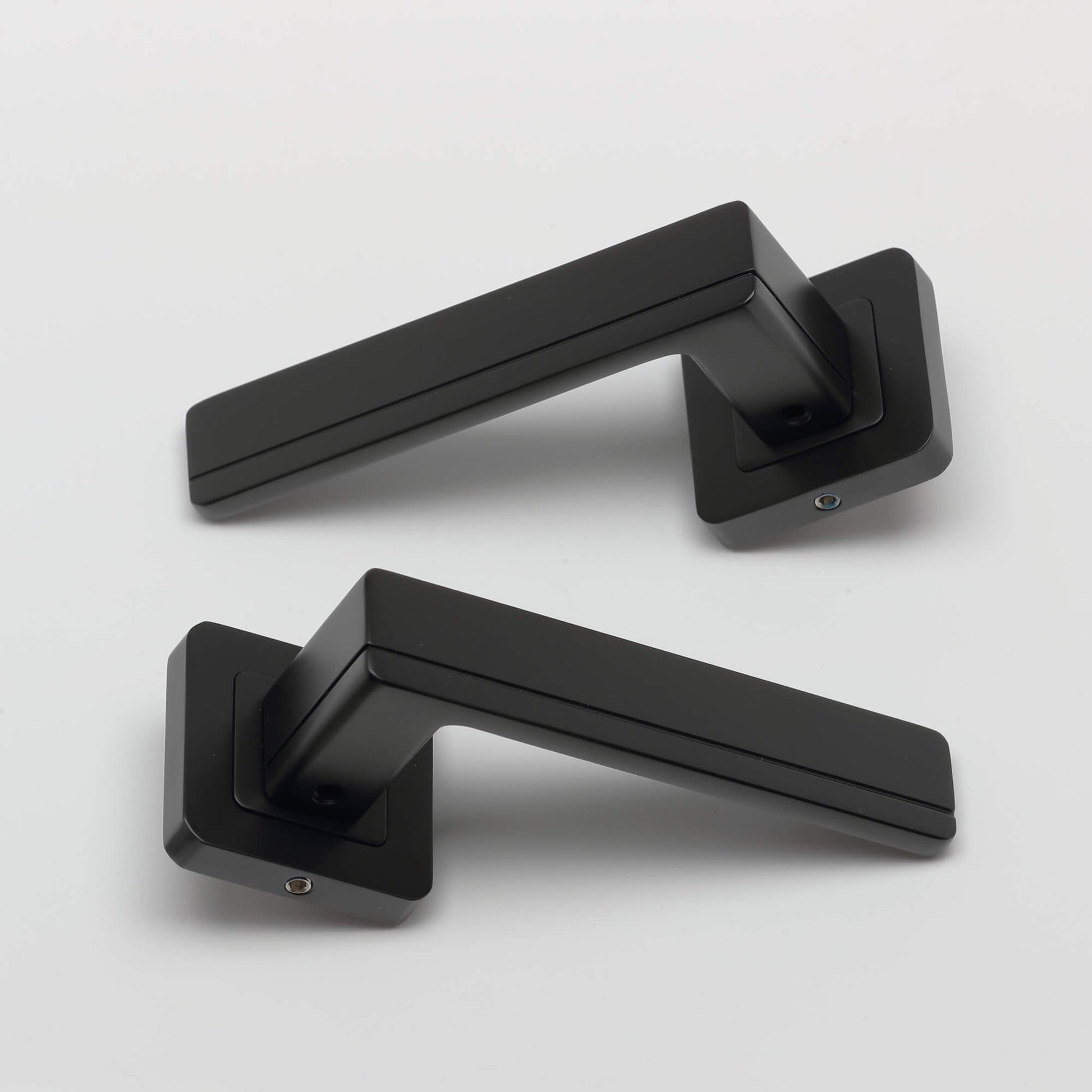 A pair of Hermes flat black square rose door handles on a light grey background.