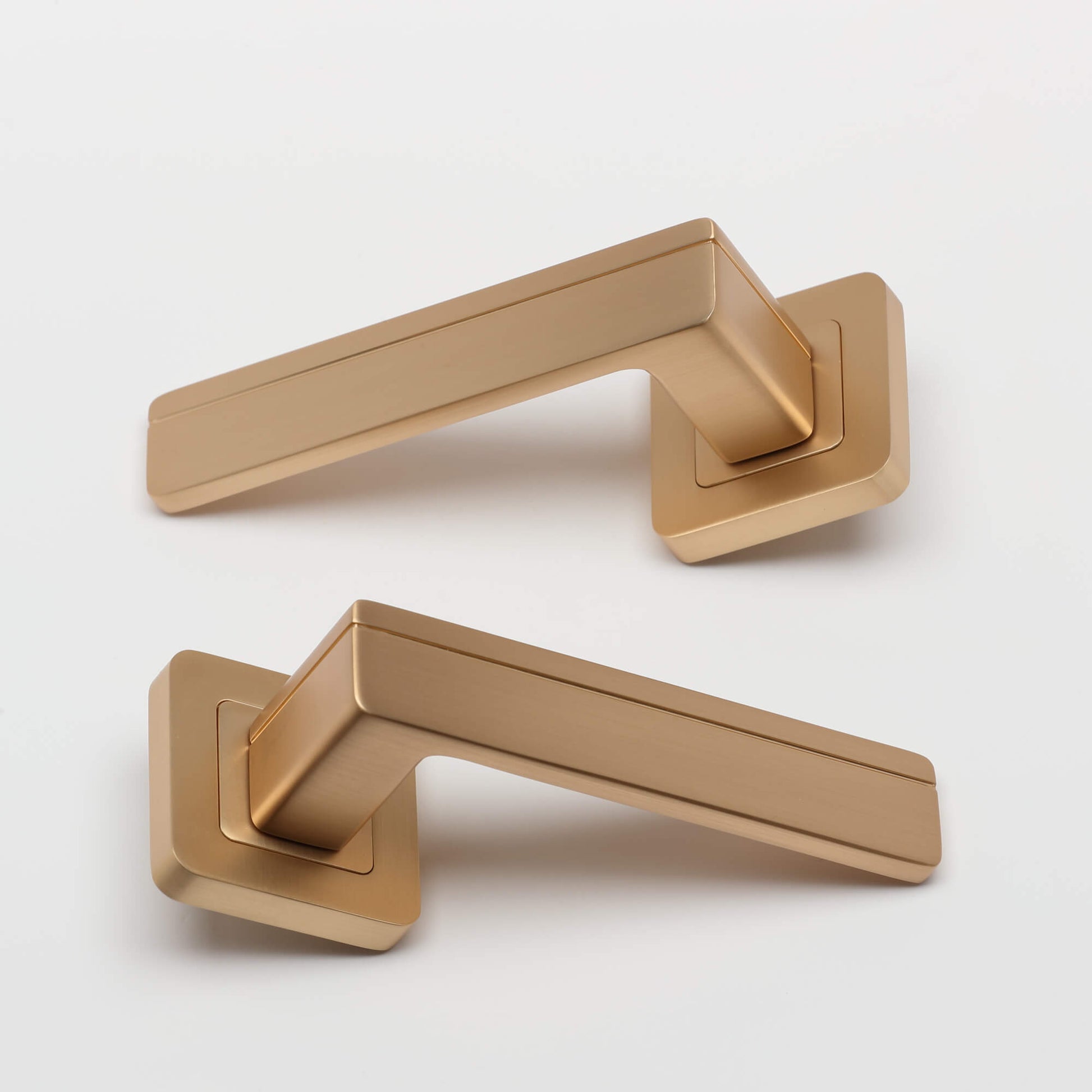 A pair of Hermes Satin Brass Square Rose door handles on a white background.