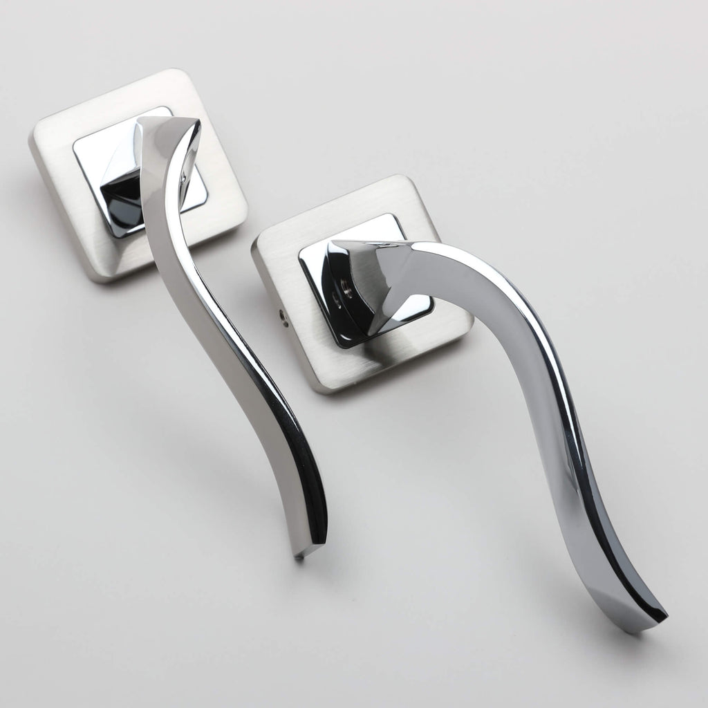 An angled view of a pair of Incus Nickel Brushed & Polished Chrome Square Rose door handles on a light grey background.
