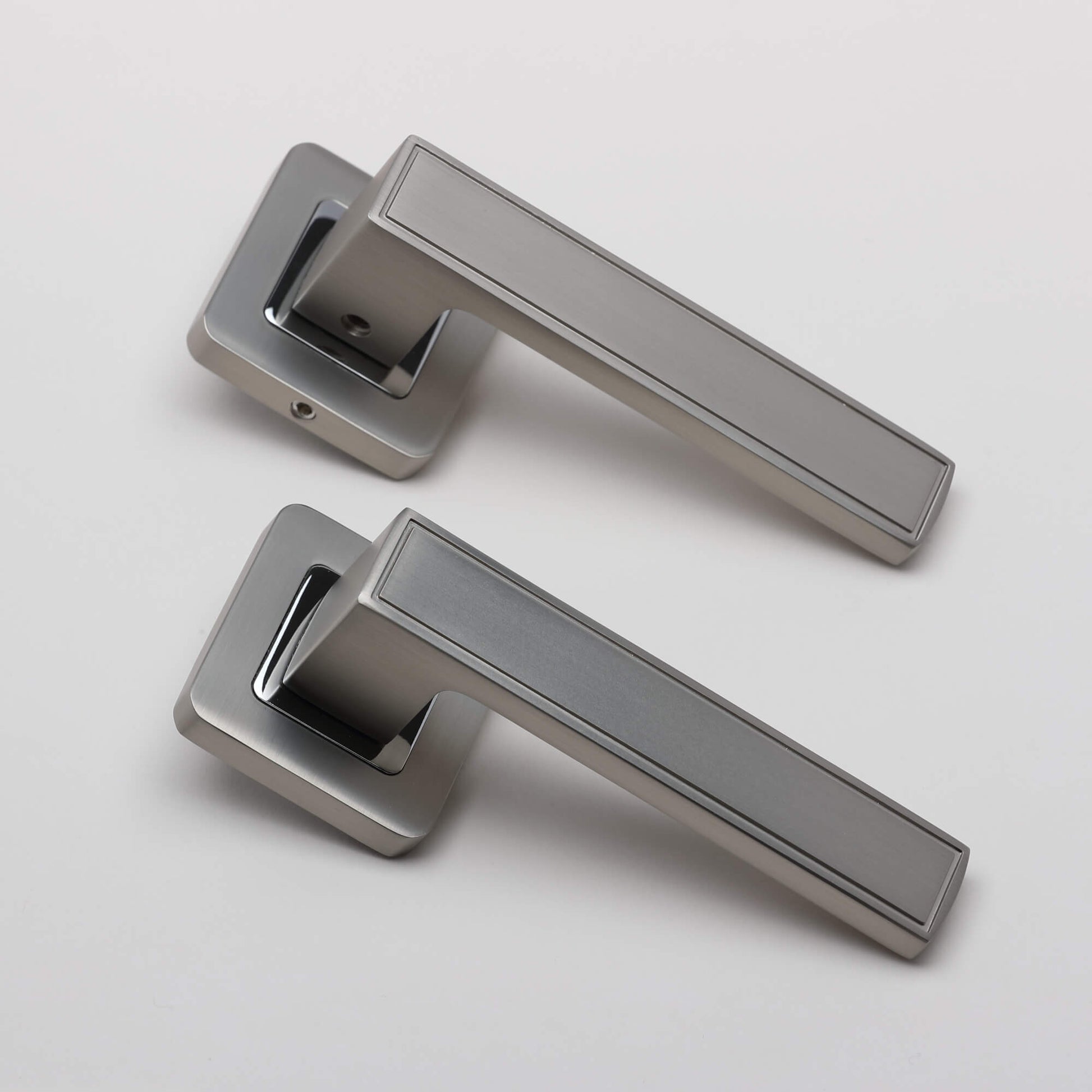 An angled view of a pair of Jupiter Matt Satin Nickel & Polished Chrome Square Rose handles on a light grey background.