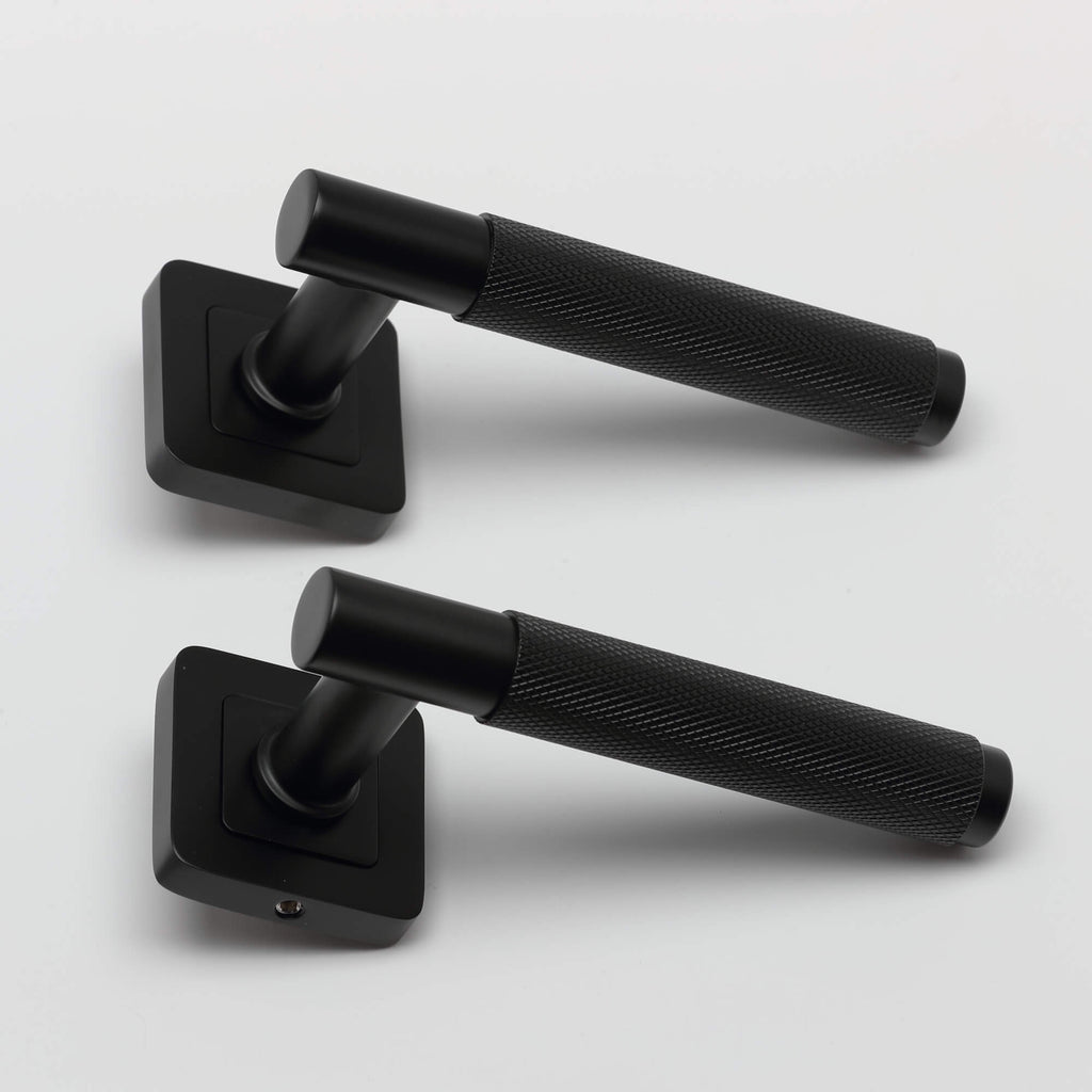 A side view of a pair of Knurled Flat Black Square Rose door handle on a light grey background.