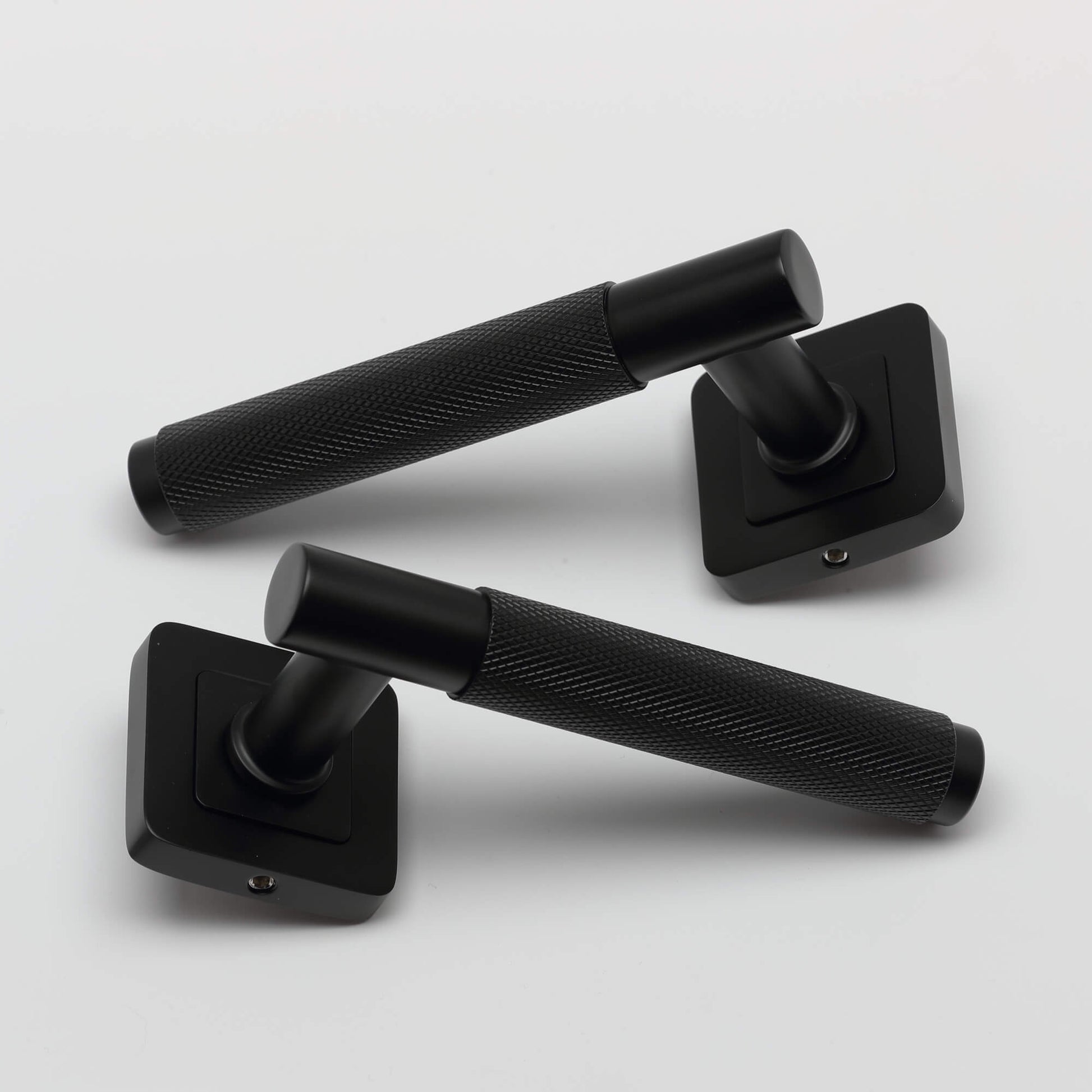 A pair of Knurled Flat Black Square Rose door handle on a light grey background.