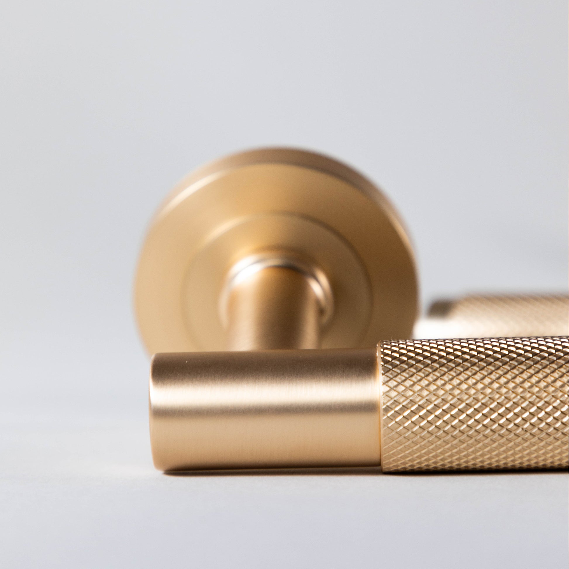 Close-up of a Knurled Satin Brass door handle on a light gray background