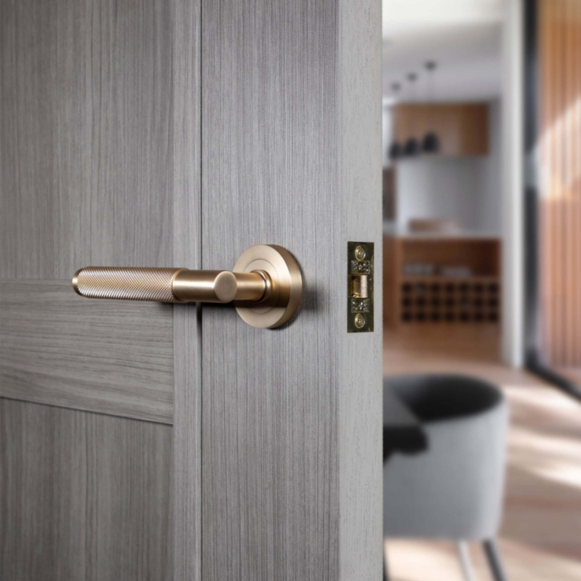 Close-up of a wooden door with a Knurled Satin Brass Handle handle, blurred interior background.