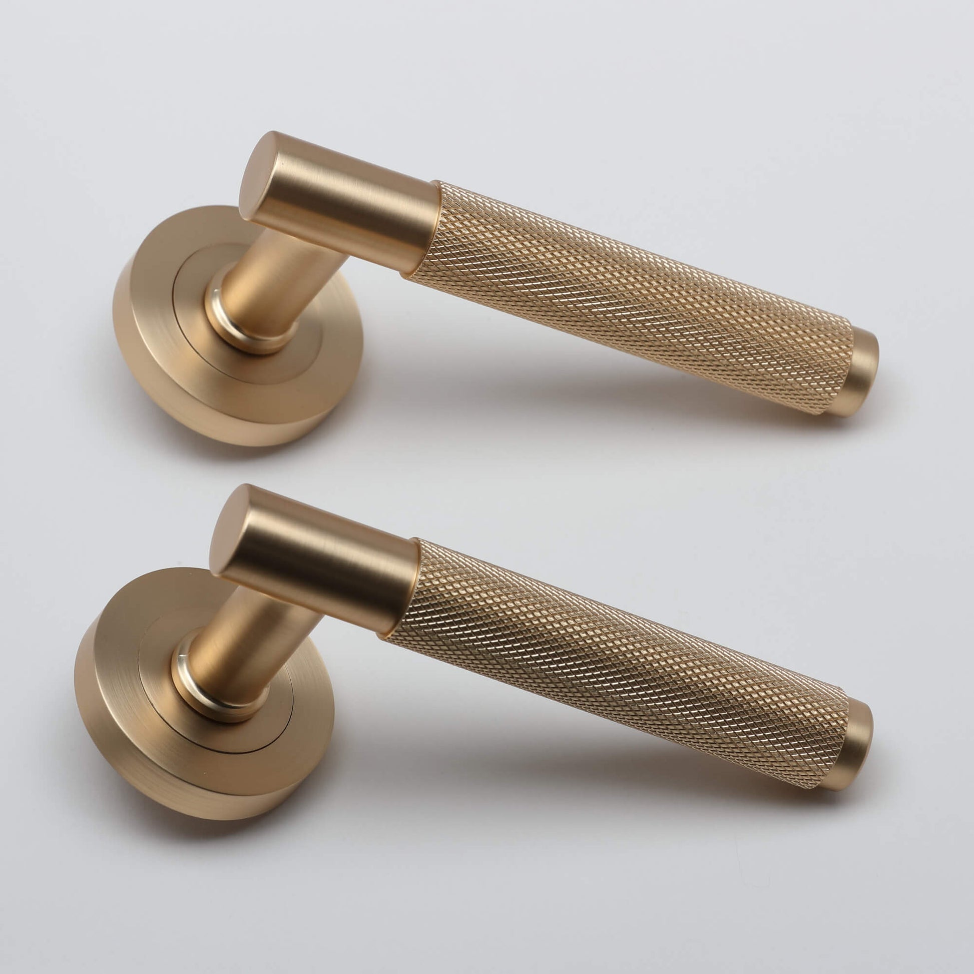 A side view of a pair of Knurled Satin Brass Handle door handles set on a light grey background.