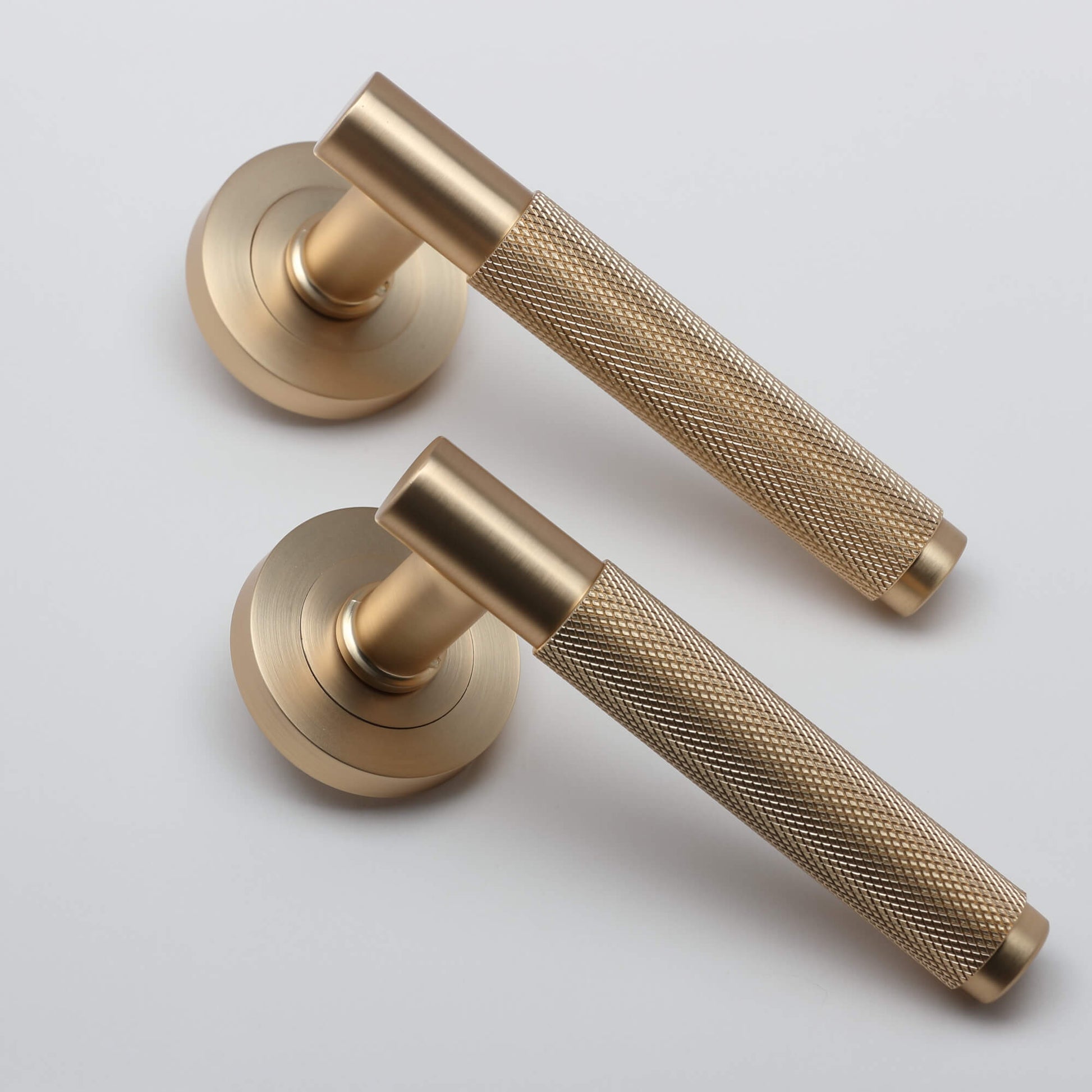 A angled view of a pair of Knurled Satin Brass Handle door handles set on a light grey background.