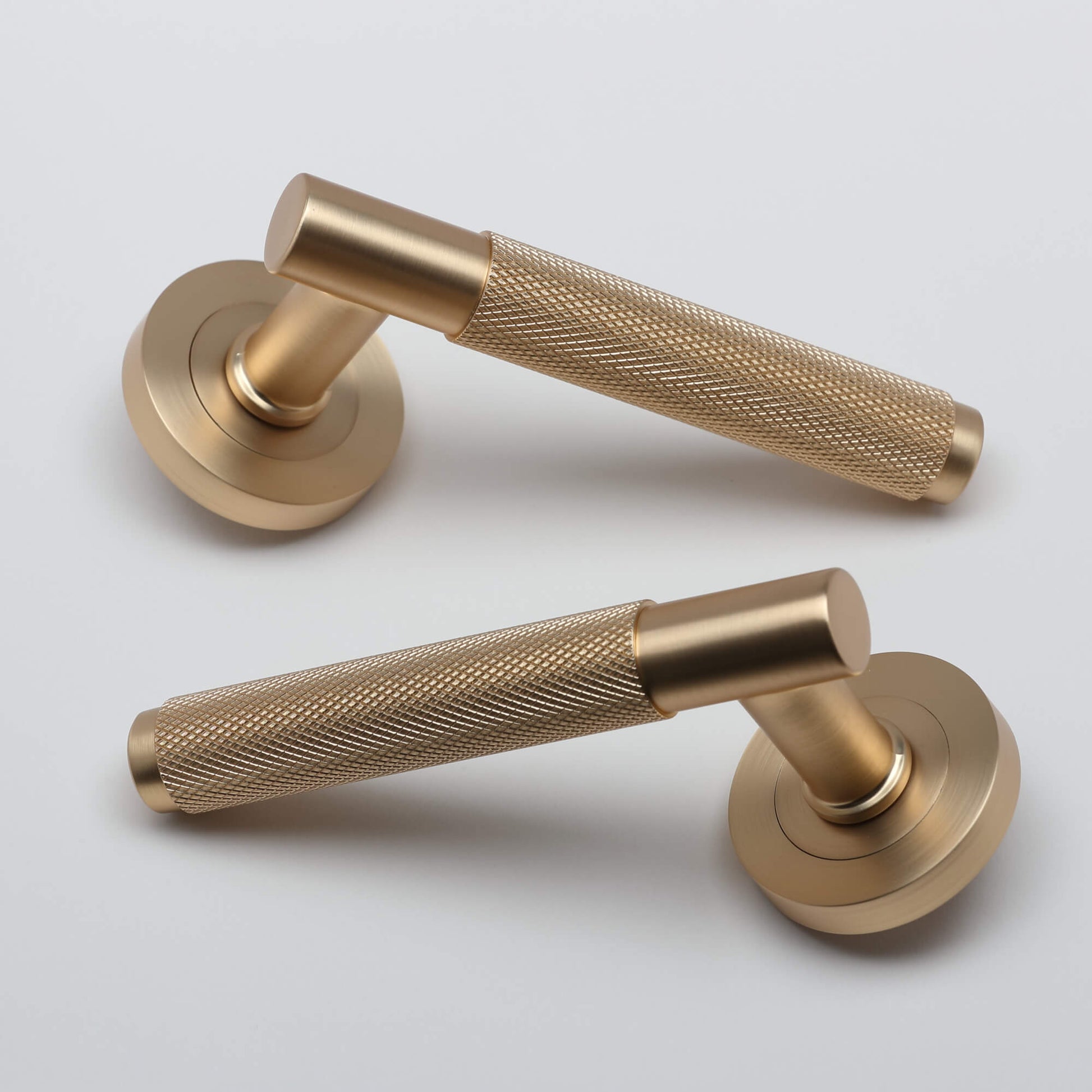 A pair of Knurled Satin Brass Handle door handles set on a light grey background.