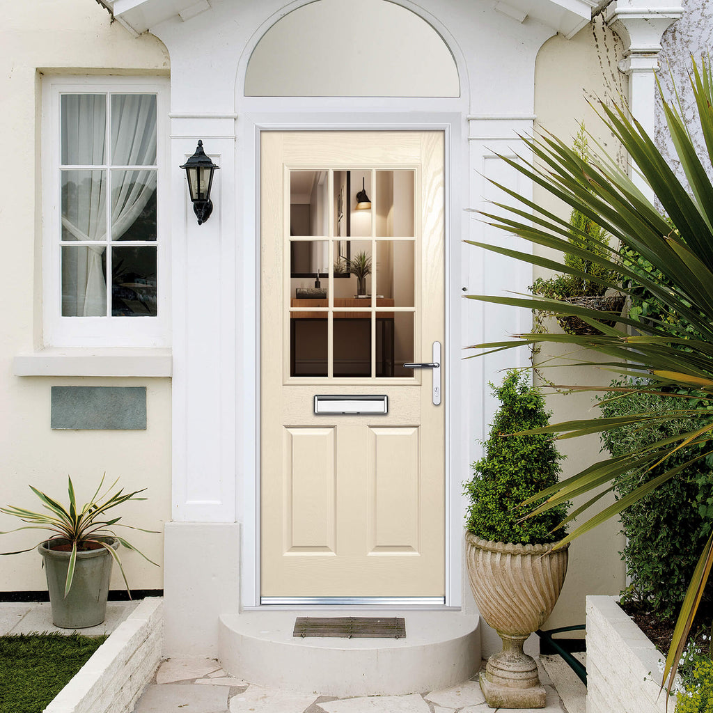 A Beige Mayfair Composite GRP front door with glass panels on a white house exterior, surrounded by plants.