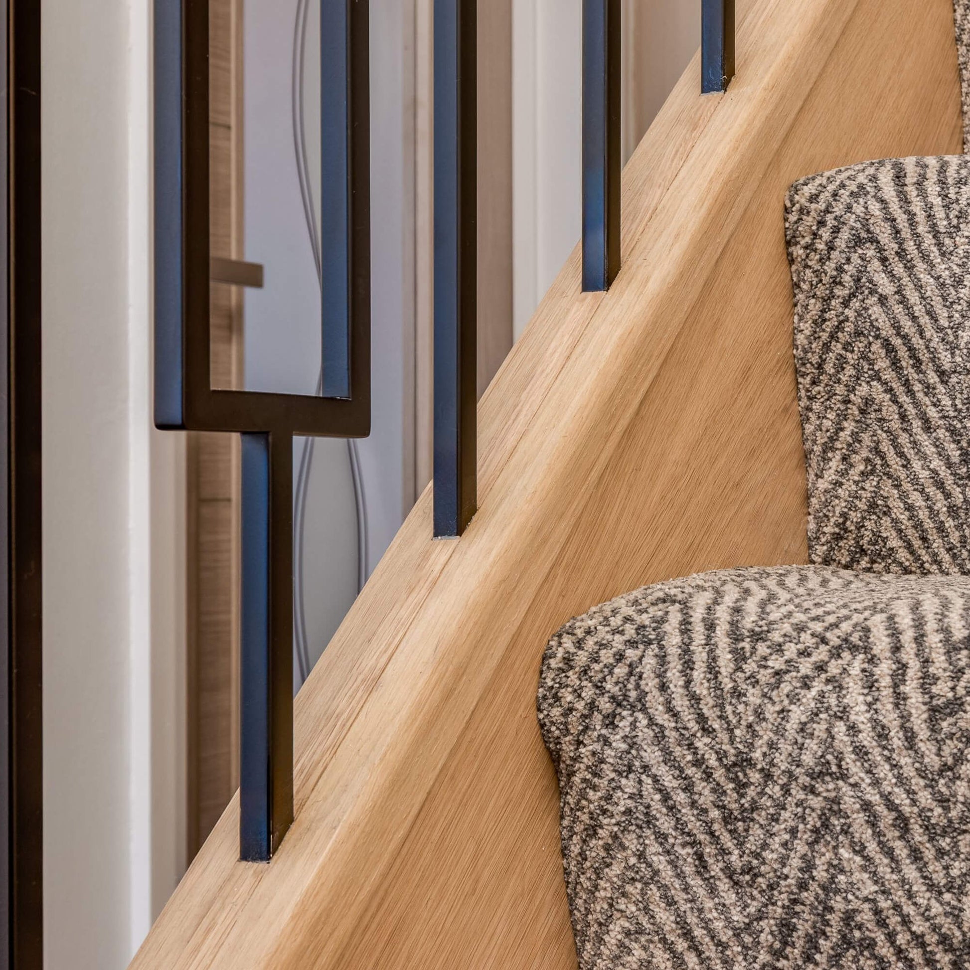 Close-up of an Oak Veneered (13mm Infill) Baserail on an oak staircase with patterned carpeting and modern railings.