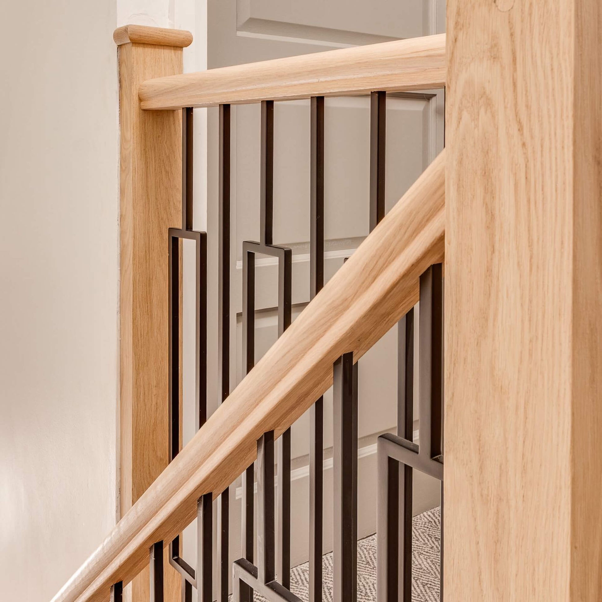 An Oak Veneered (13mm Infill) Handrail on a Wooden staircase with black rectangle spindles in a home interior setting.