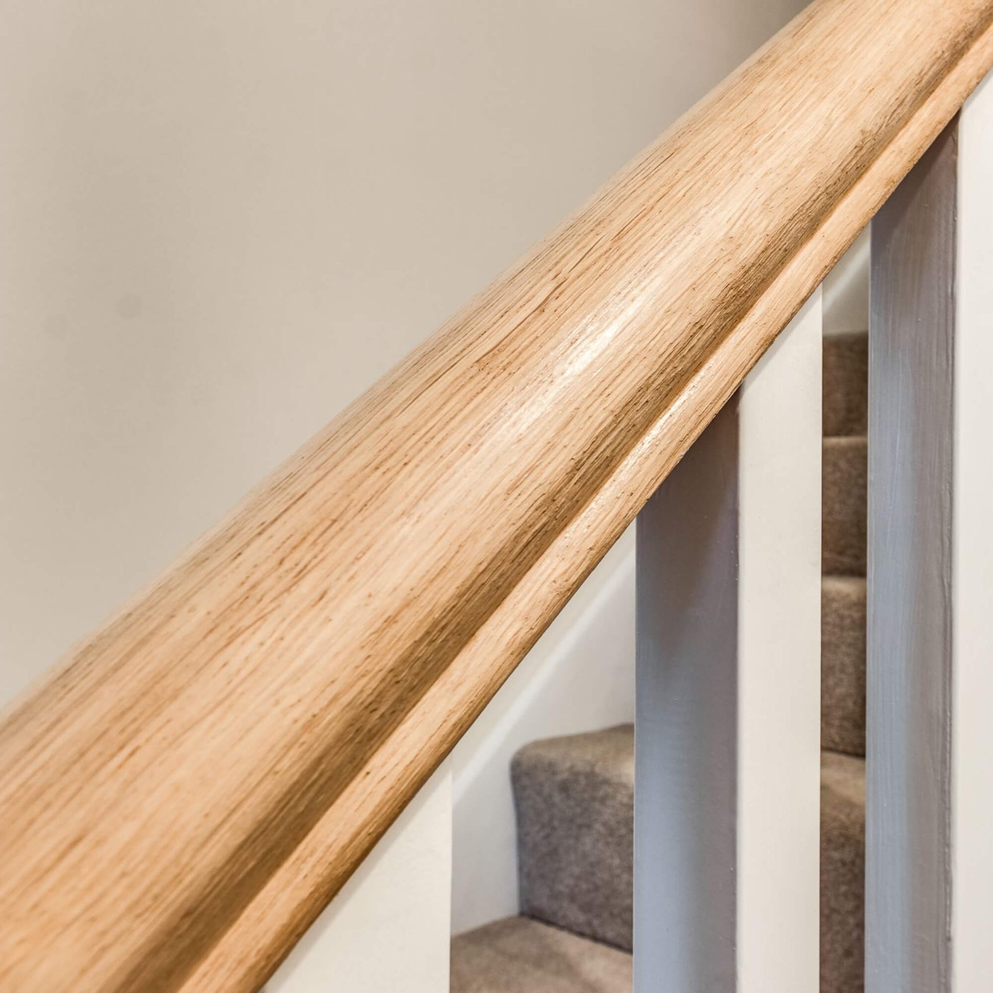 Close-up of an Oak Veneered Standard (41mm) Handrail on a staircase with a neutral background.