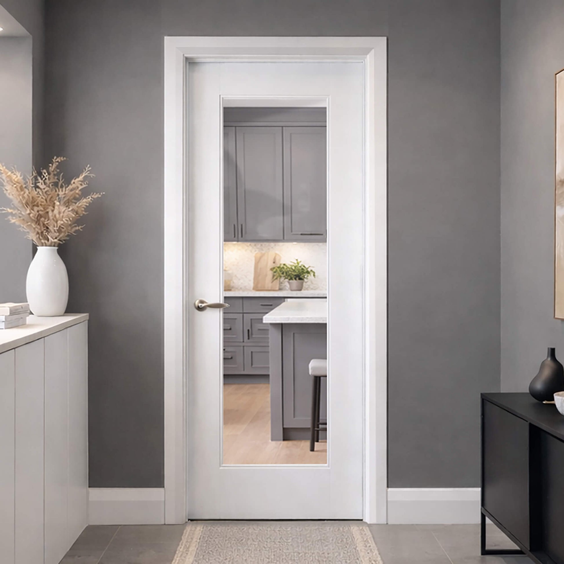 A Shaker White Primed 1 Lite Pre-Glazed Door in a hallway, with gray walls and furniture, looking into a kitchen setting.