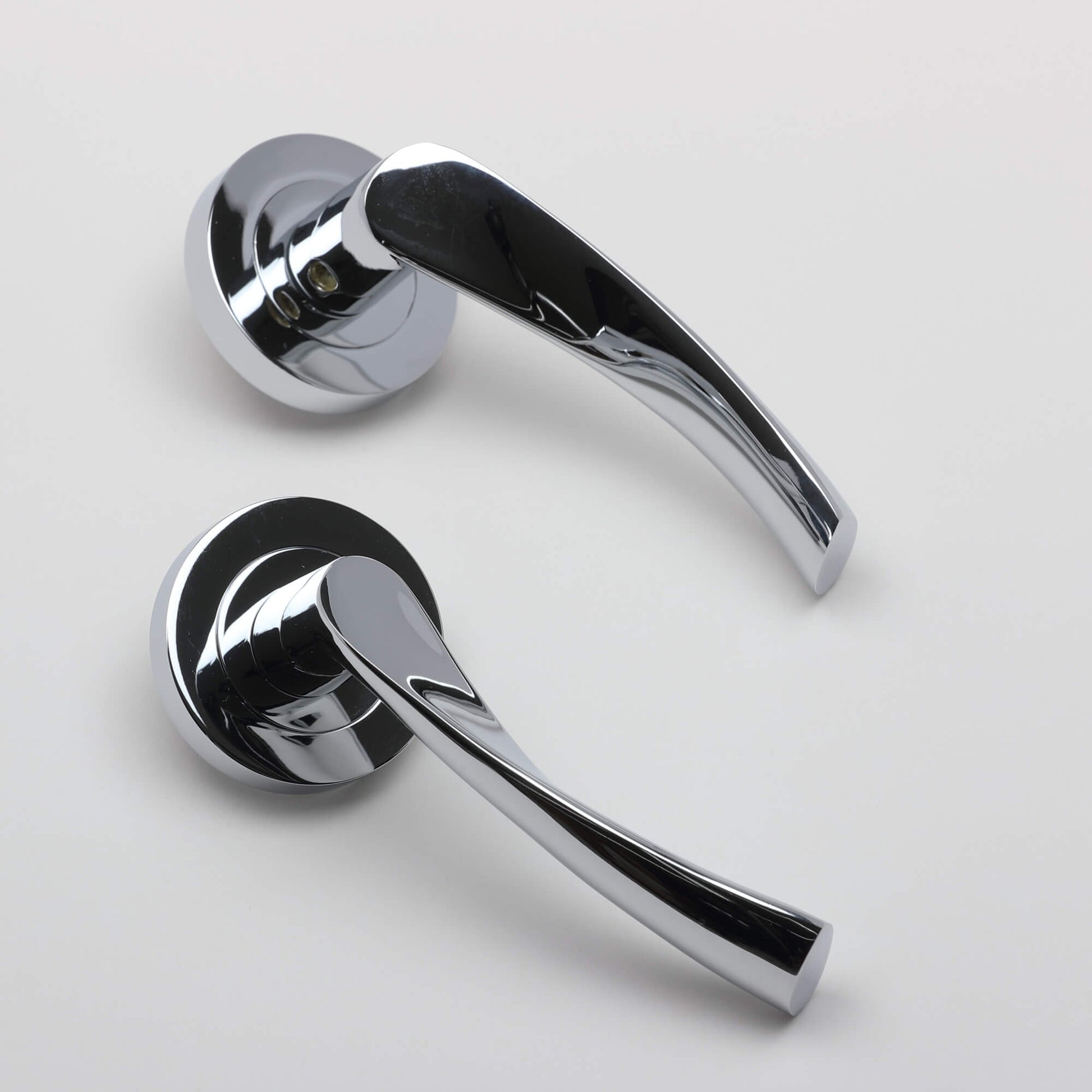 An angled view of a pair of Trade Range Polished Chrome door handles on a grey background.
