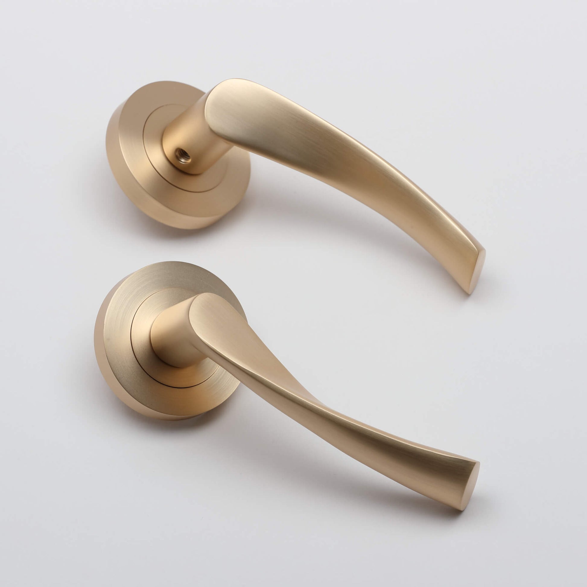 An angled view of a pair of Trade Range Satin Brass Handles on a grey background.