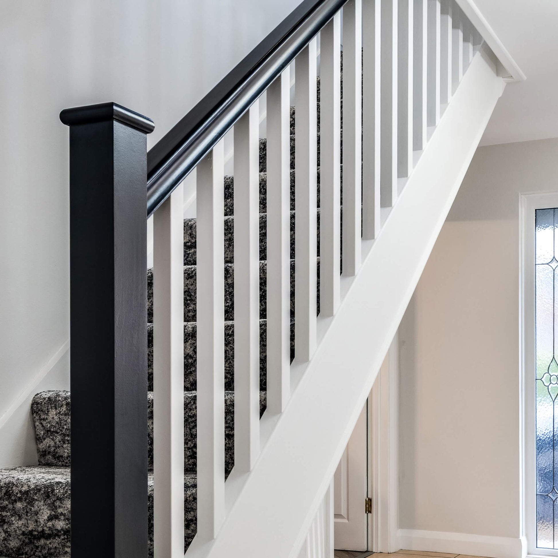 Staircase with black newel post and white primed blank spindles in a home interior.