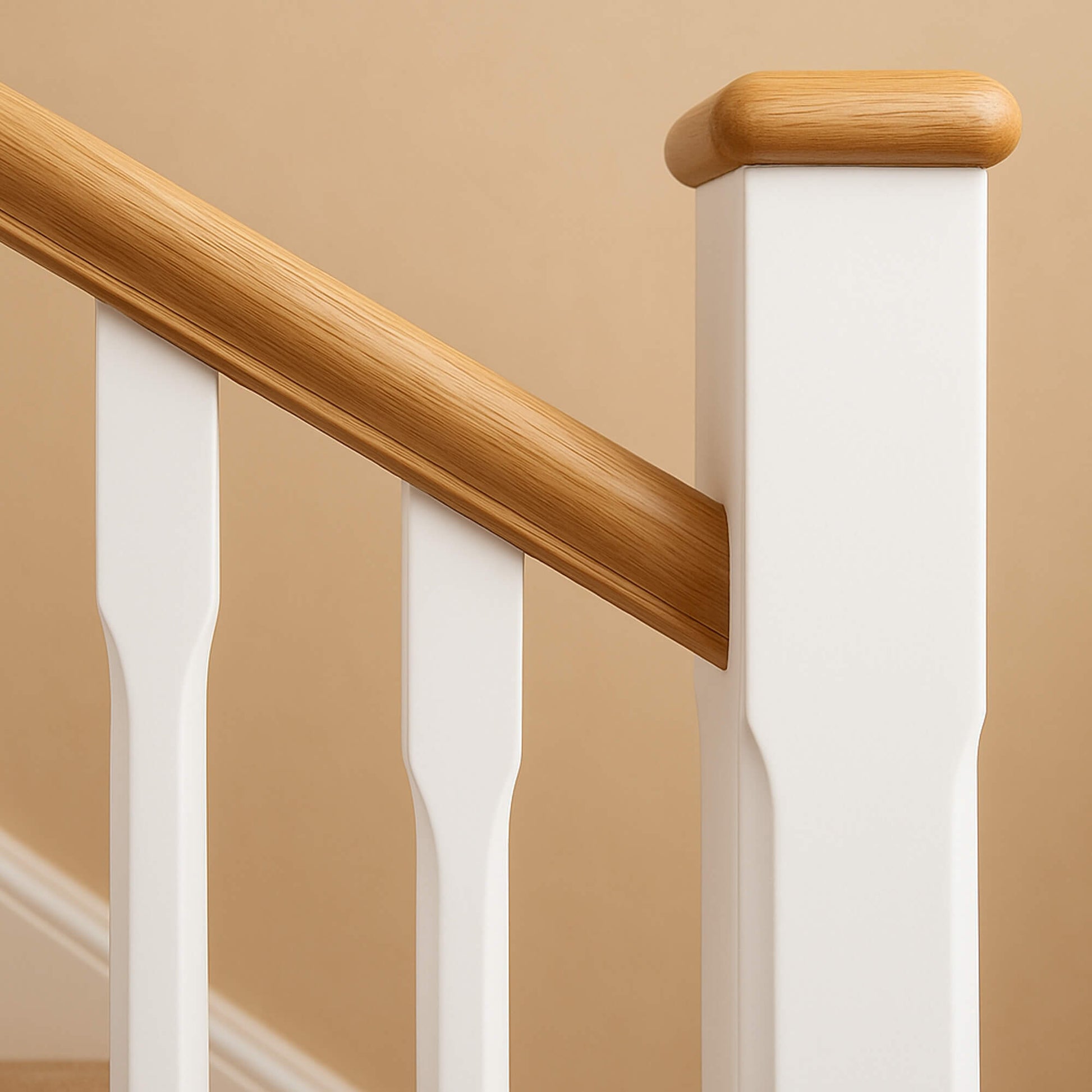 Close-up of a wooden handrail and white balusters with an Oak Flat Newel Cap against a beige wall.