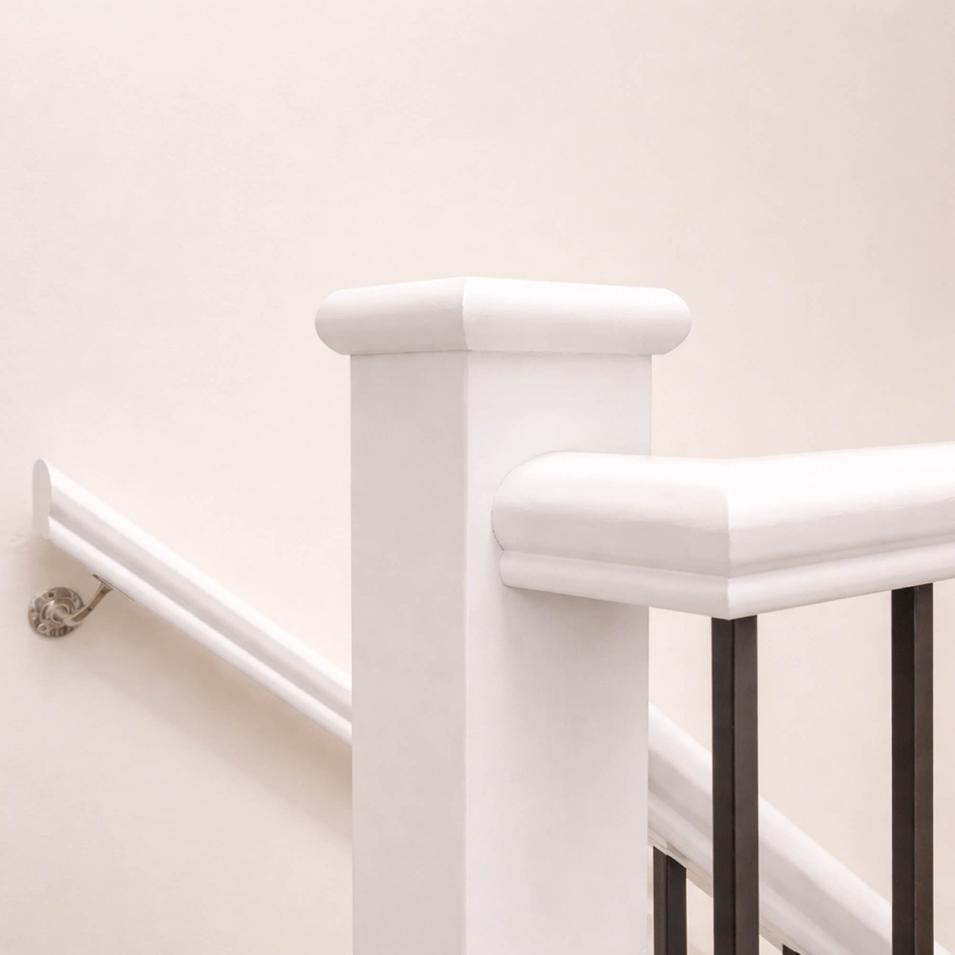 White Primed Handrail (13mm Infill) with a white primed blank newel post with black blank spindles against a beige wall.